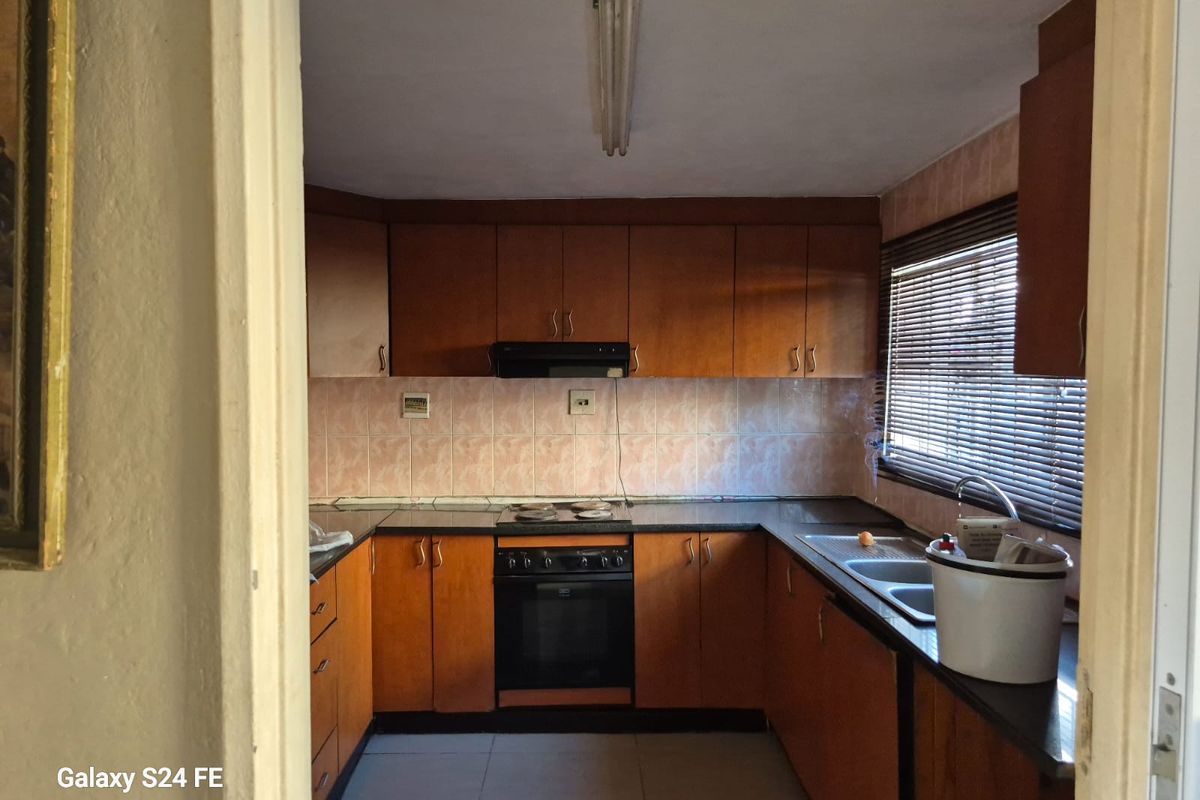 A functional kitchen featuring wood-tone cabinetry, built-in oven and hob, tiled backsplash, and double sink, offering potential for a modern renovation.