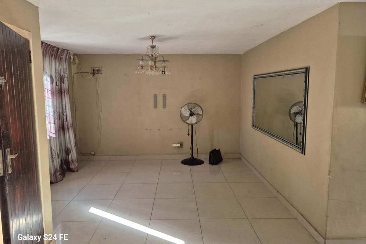 An empty living room featuring tiled flooring, a crystal chandelier, and a large wall-mounted mirror, offering a blank canvas for interior design updates.