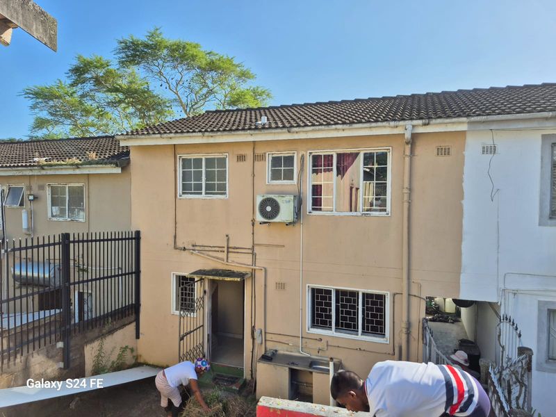 Rear elevation of a two-story residential property featuring tiled roofing, security bars, and an external sink area requiring maintenance.