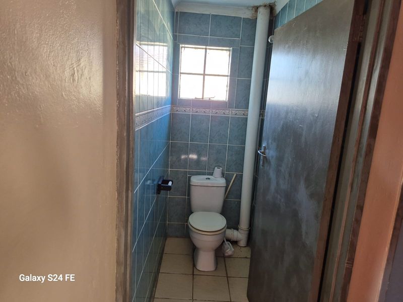 A compact bathroom featuring blue wall tiling, ceramic floor tiles, and an exposed plumbing pipe.