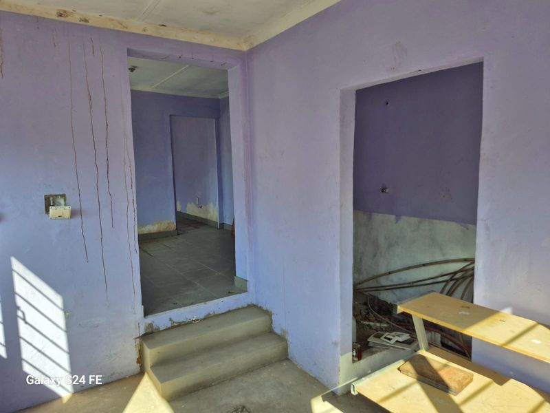 An interior hallway area showing significant signs of wear, including water damage, peeling paint, and exposed plumbing, requiring substantial renovation and repair.