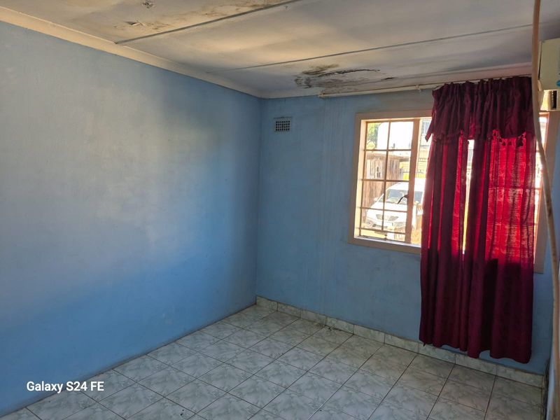 An empty bedroom featuring tiled flooring and security bars on the window, currently showing significant signs of ceiling water damage and wear.