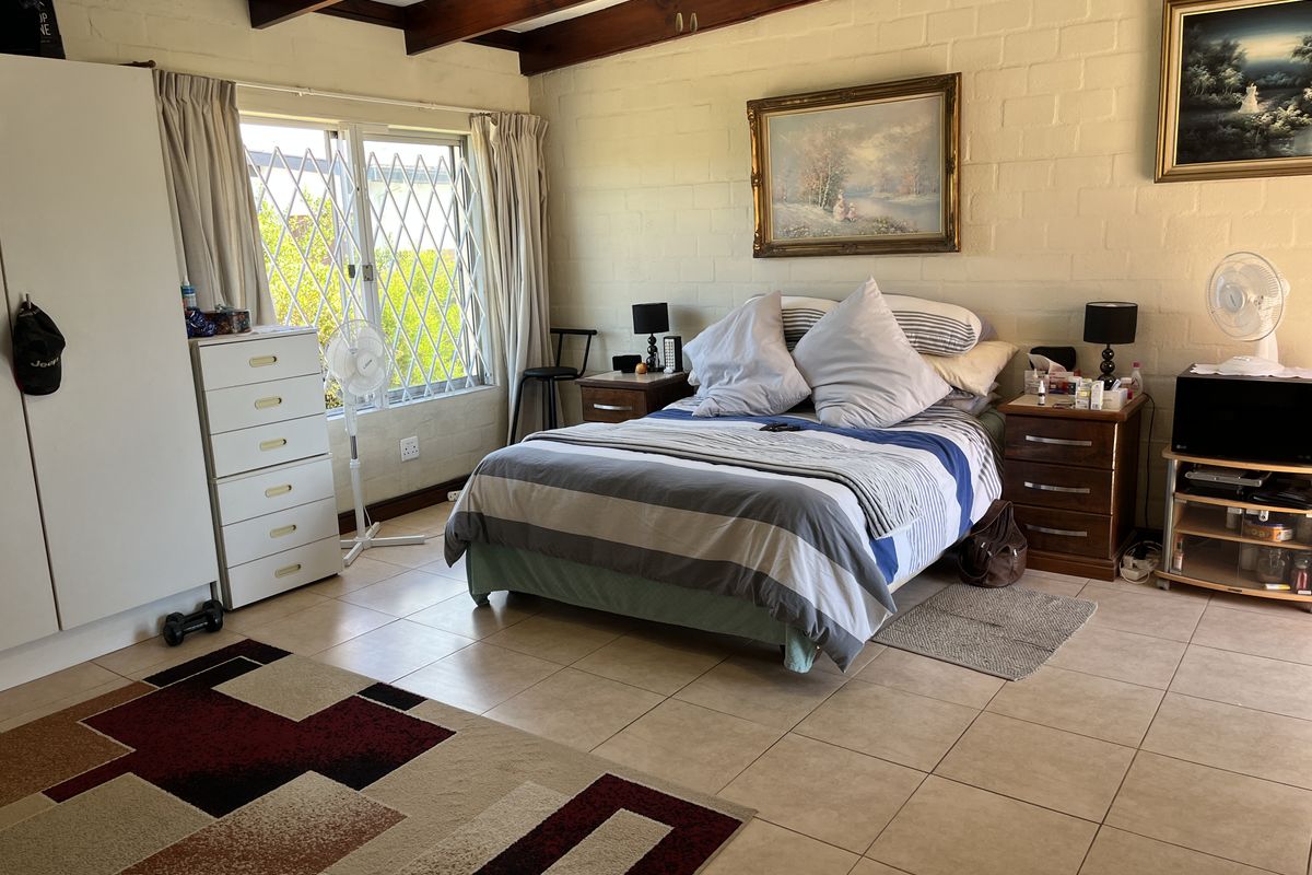 A spacious bedroom featuring exposed timber ceiling beams, tiled flooring, and masonry block walls, providing a solid foundation for modern interior updates.
