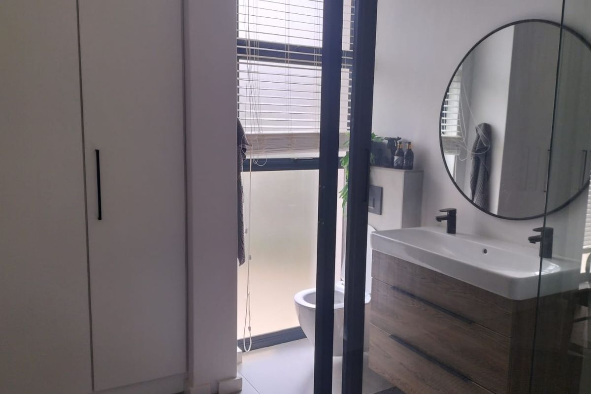 Modern bathroom featuring a wood-finish vanity with black tapware, wall-mounted toilet, and ample built-in storage cupboards.