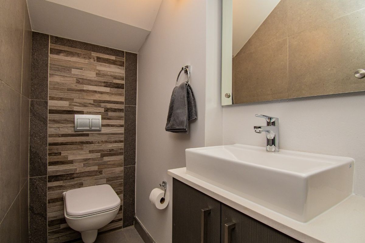Modern guest bathroom featuring a wall-mounted toilet with concealed cistern, a vessel sink vanity, and contemporary tiled feature wall.