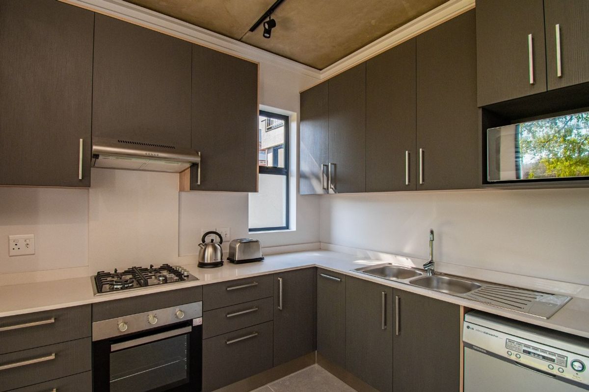 Modern kitchen featuring dark cabinetry, stone countertops, a built-in gas hob, oven, extractor fan, and a double sink with integrated dishwasher space.