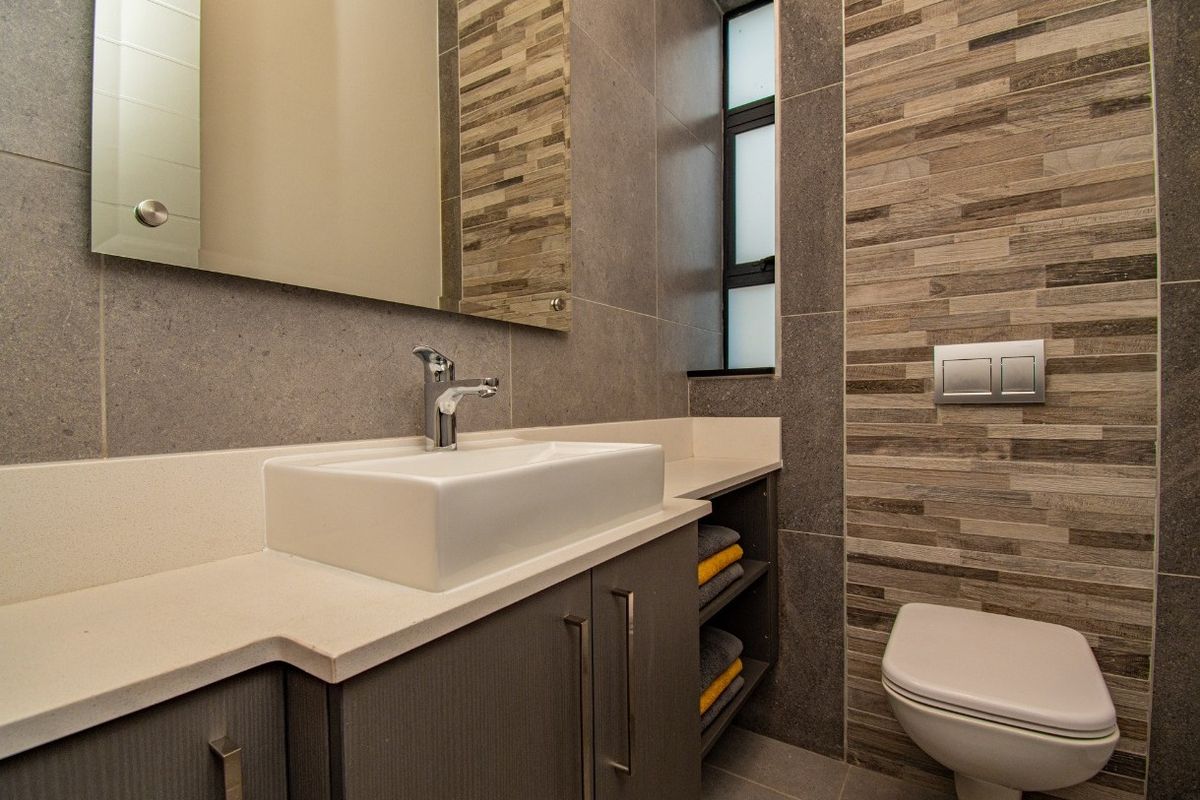 Modern bathroom featuring a wall-mounted toilet, stone-topped vanity with integrated basin, and textured feature tiling.