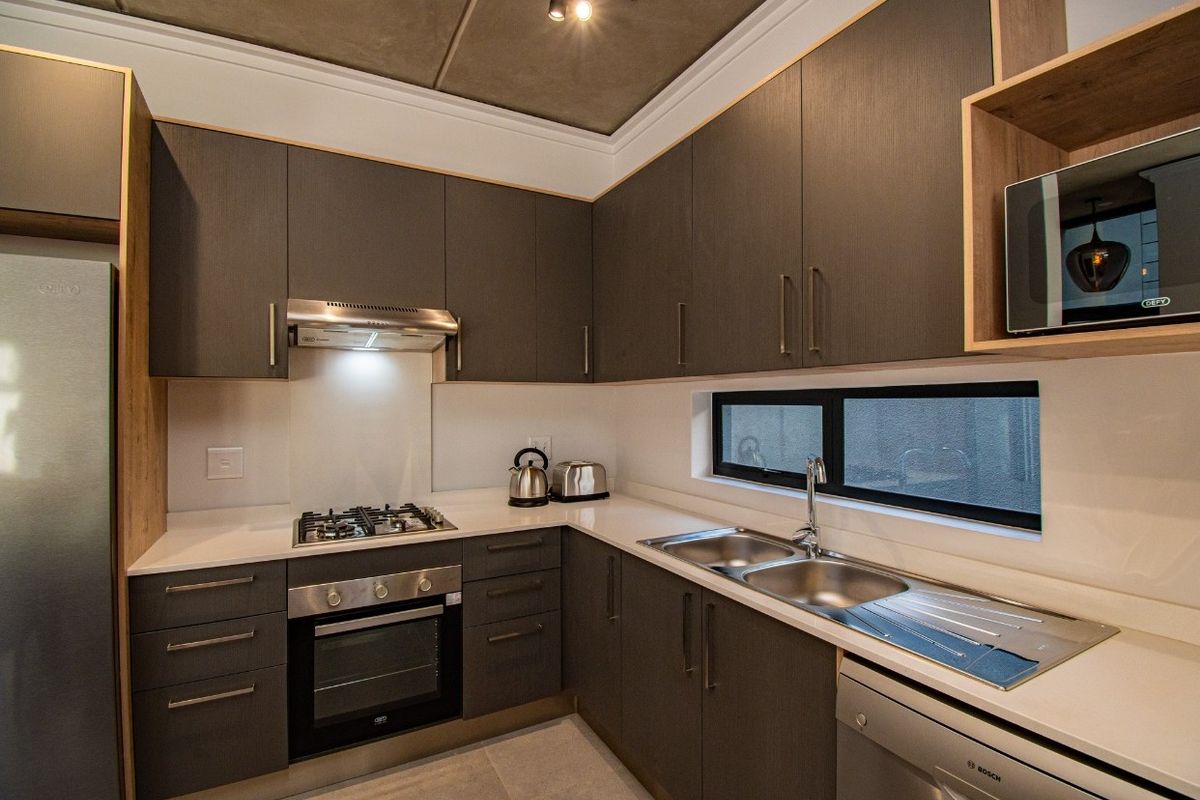 Modern kitchen featuring dark wood cabinetry, stone countertops, stainless steel gas hob, built-in oven, extractor fan, and a double sink with a window view.
