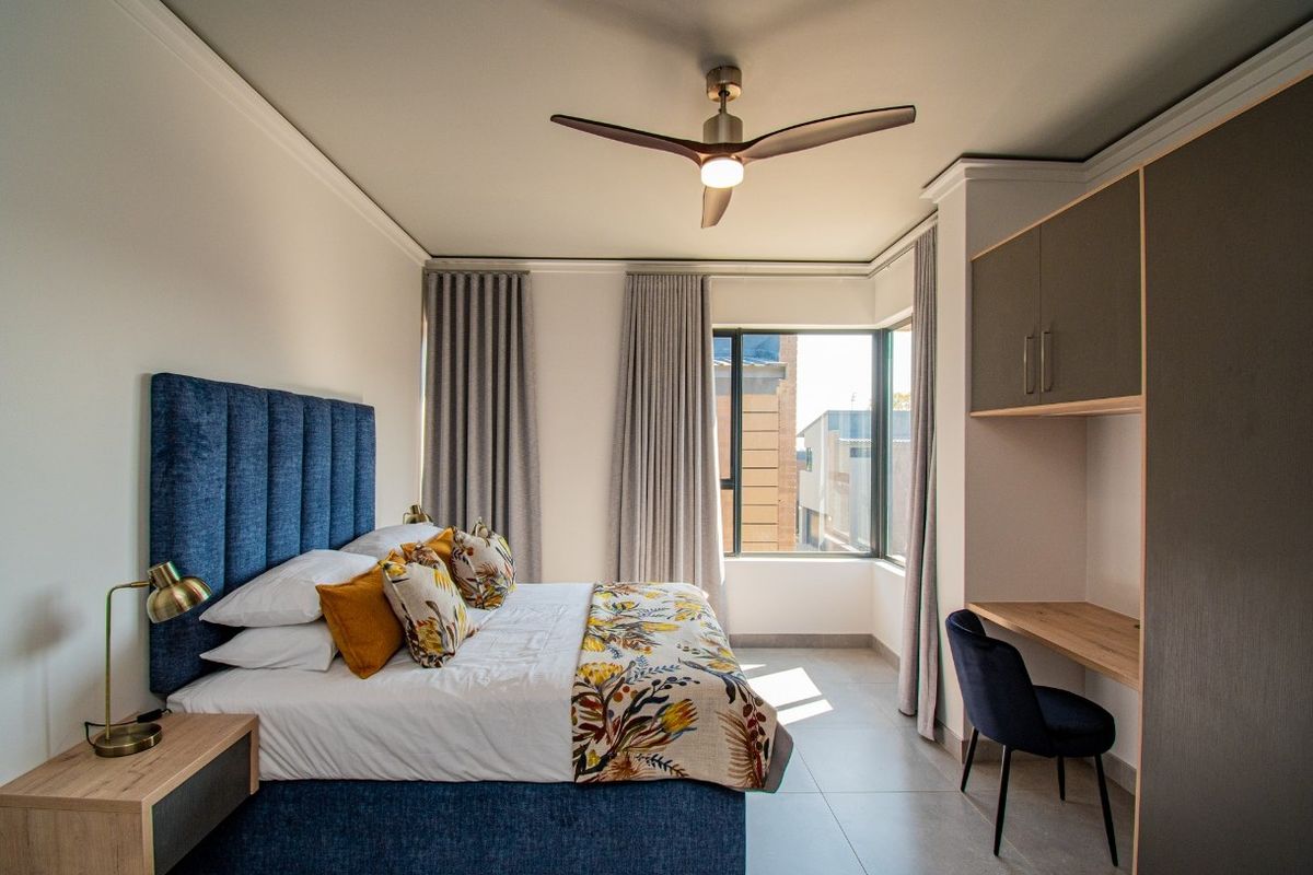 A modern bedroom featuring tiled flooring, a built-in desk with overhead cabinetry, and a ceiling fan, offering a clean and contemporary living space.