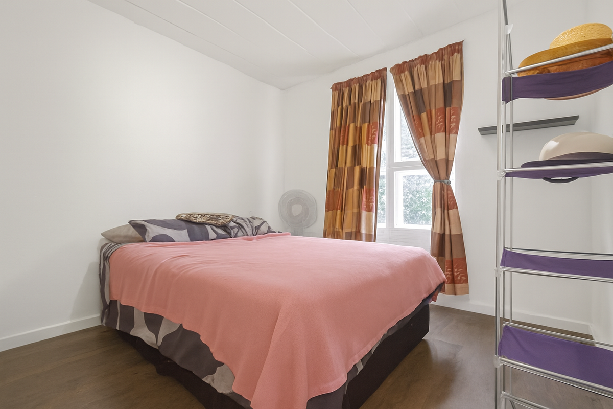 A simple bedroom featuring wood-look flooring, a window with curtains, and a plain white ceiling.