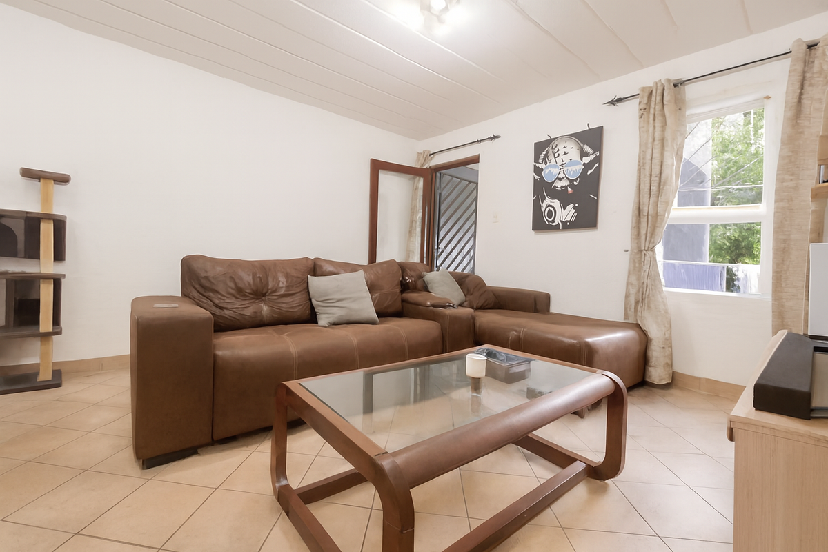 A living room featuring tiled flooring, a window with curtain rods, and a doorway leading to an exterior area.
