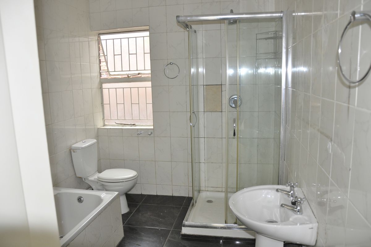 A functional bathroom featuring a white bathtub, a separate glass-enclosed shower, a pedestal basin, and a toilet with tiled walls and flooring.