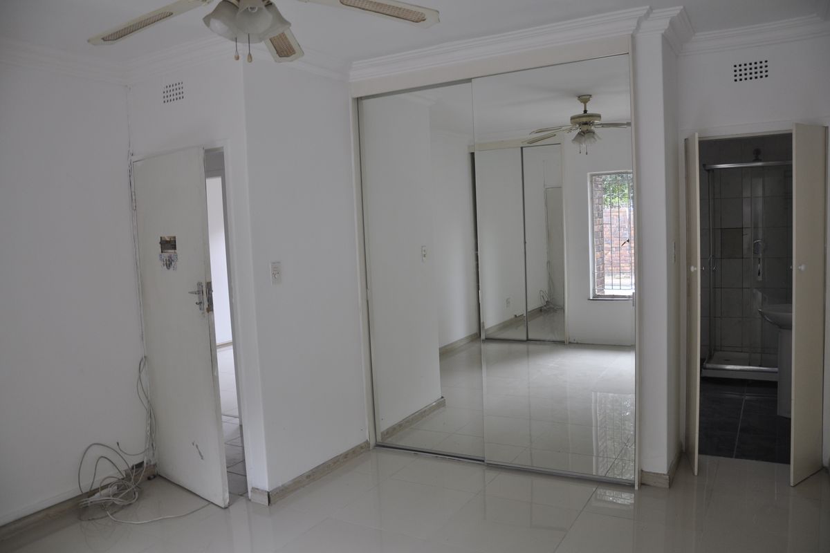 A bedroom featuring tiled flooring, built-in mirrored sliding wardrobes, a ceiling fan, and an en-suite bathroom.