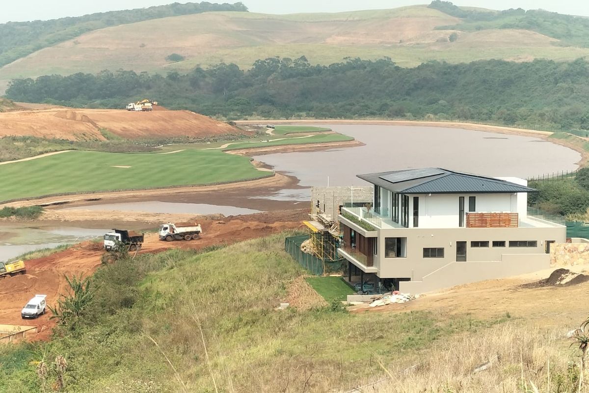 Aerial view of a modern multi-level residence situated on a large estate with surrounding construction and natural landscape views.
