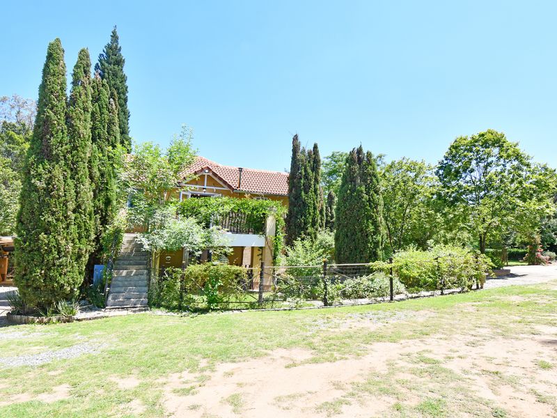 Rear view of a two-story house featuring a balcony, concrete staircase, and established garden with mature trees and lawn.