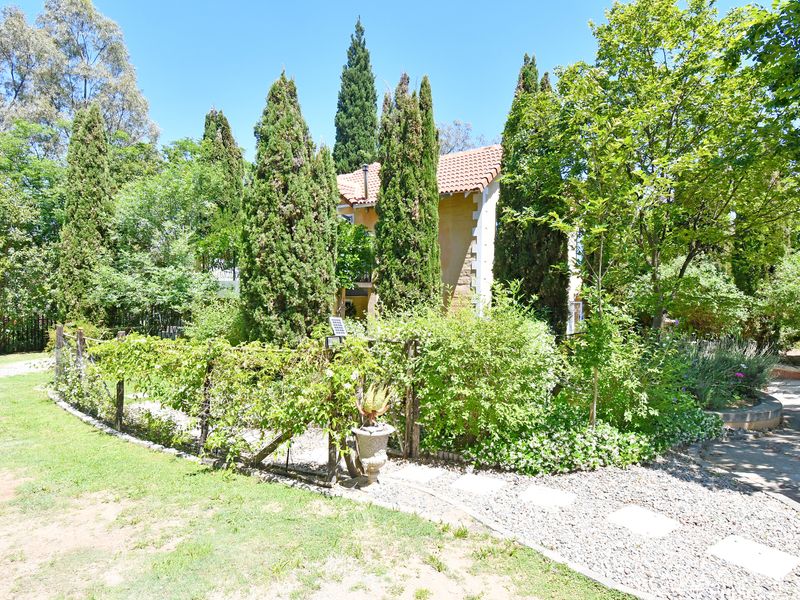 A view of the rear garden featuring mature cypress trees, a gravel pathway, and the side elevation of the house with stone detailing.
