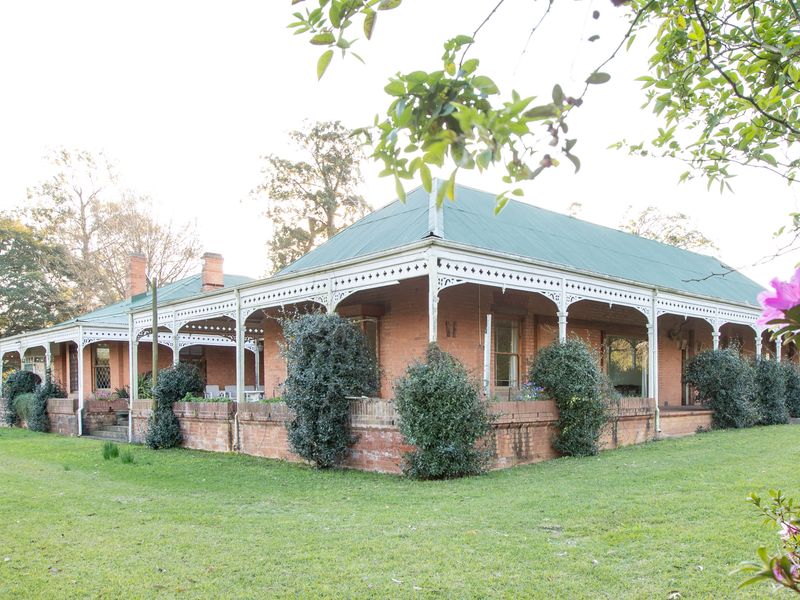 A charming historic brick home featuring a wrap-around veranda with decorative timber fretwork, set within a spacious garden.