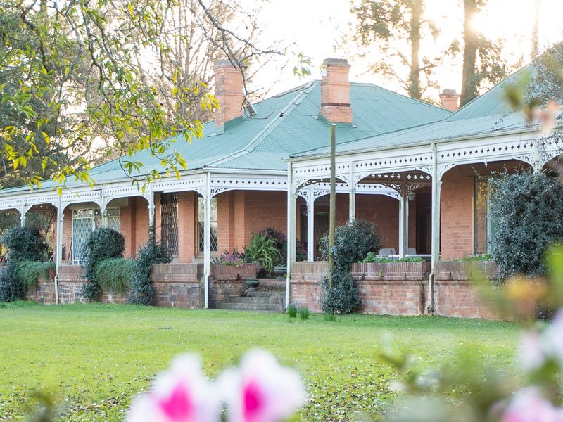 A charming historic brick residence featuring a wrap-around veranda with decorative ironwork, set within a spacious garden.