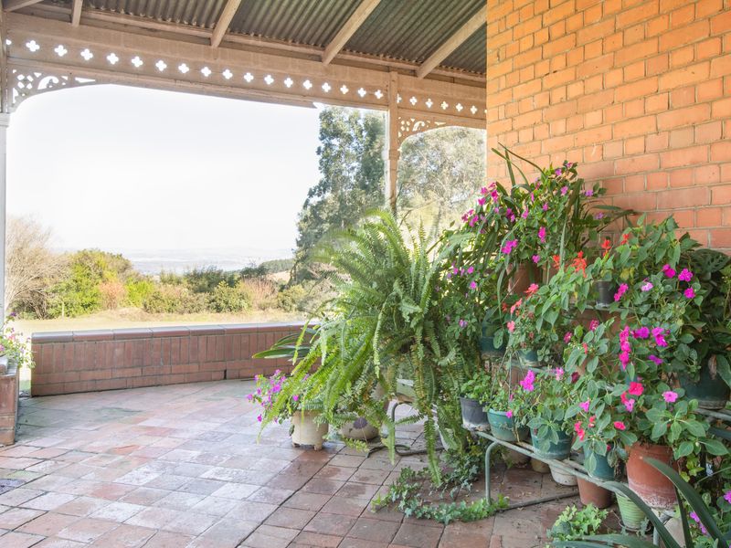 A covered outdoor patio featuring brick flooring, decorative timber fretwork, and a low brick retaining wall with scenic landscape views.