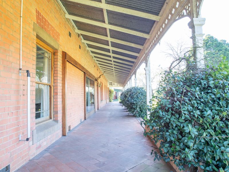 A long, covered veranda featuring classic exposed brickwork, terracotta tiling, and decorative timber fretwork, offering a traditional outdoor living space.