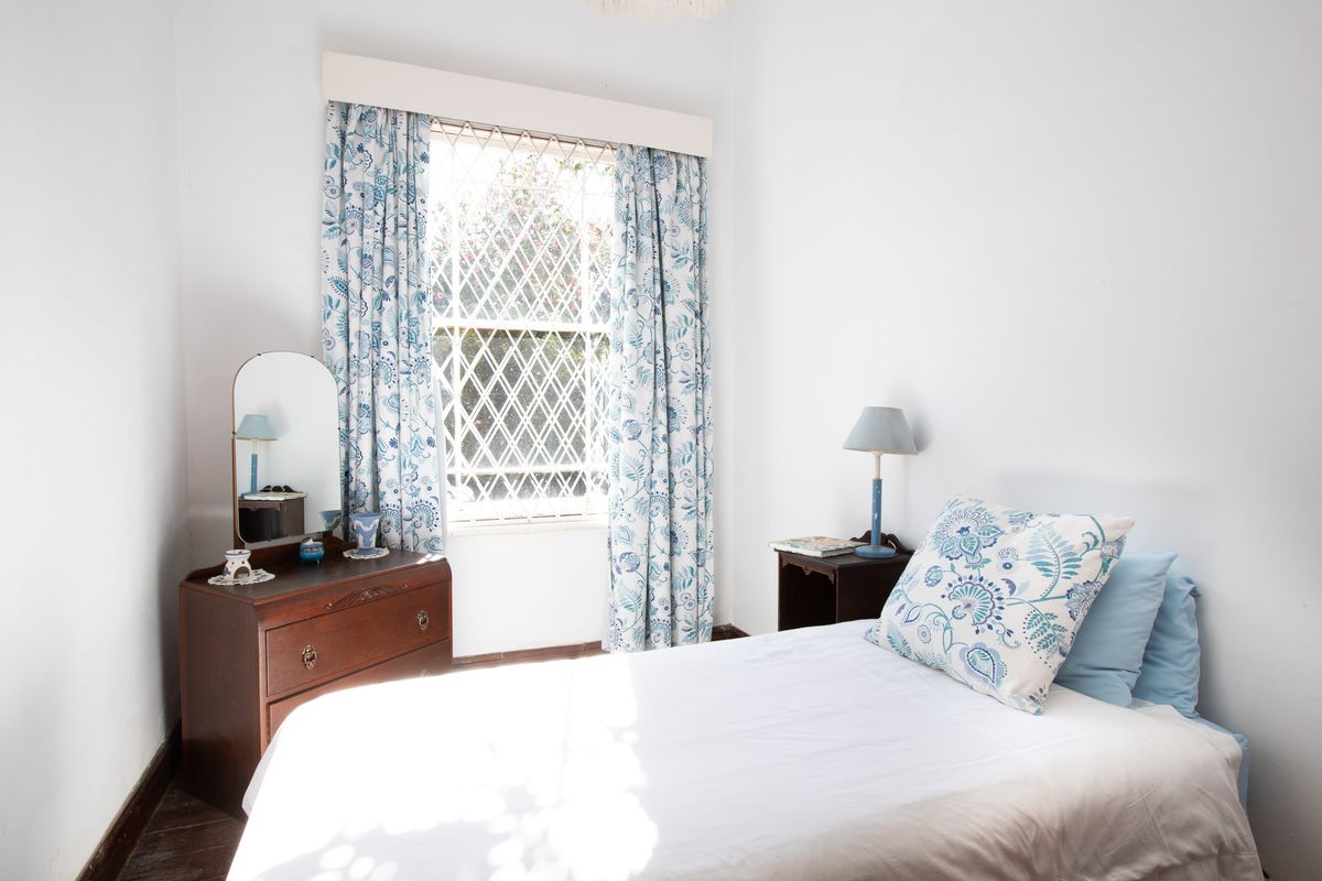 A cozy bedroom featuring timber flooring and a window fitted with a diamond-pattern security grille.