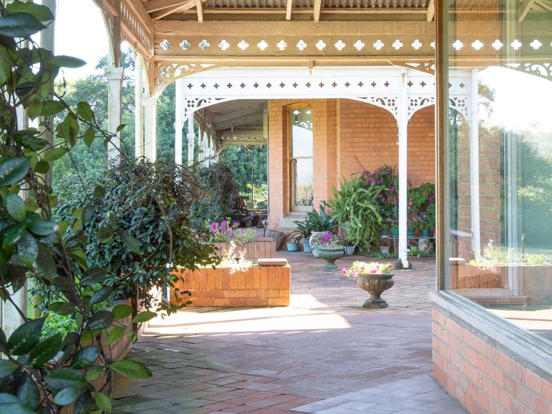 A covered outdoor patio featuring traditional timber fretwork, brick paving, and built-in brick planter boxes, offering a classic veranda aesthetic.