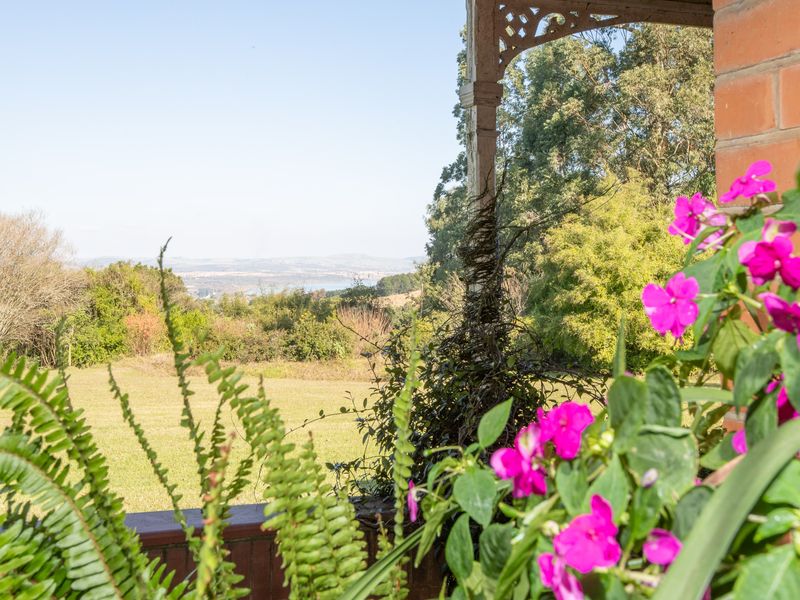 A covered patio area featuring decorative timber fretwork and brick detailing, offering expansive views over the garden and surrounding landscape.