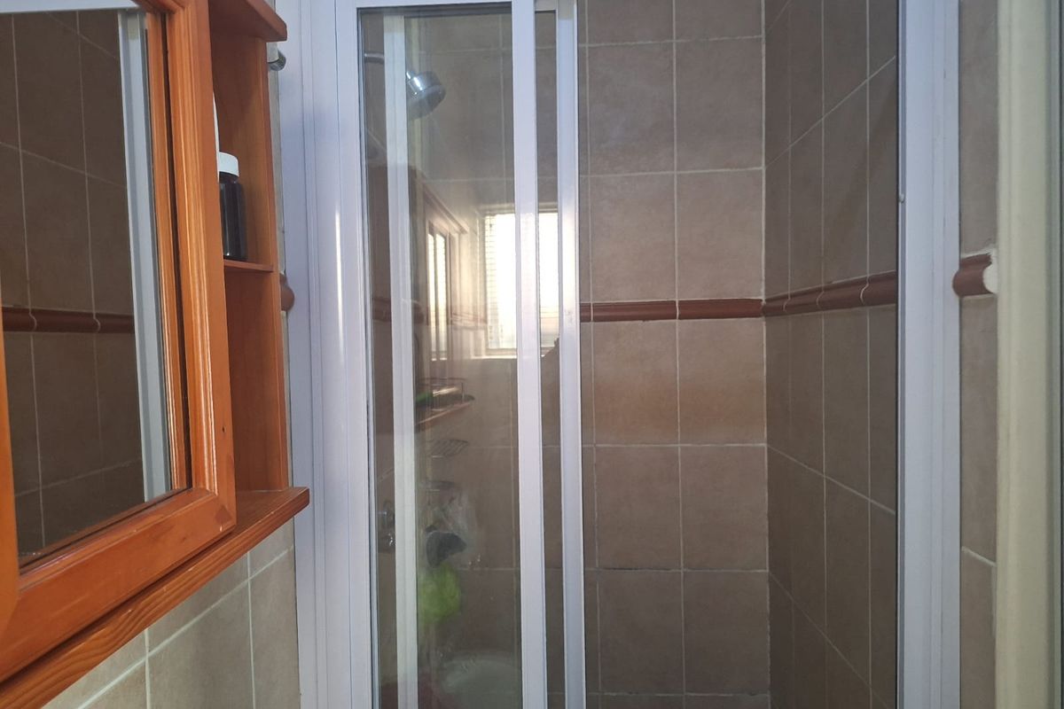 A functional bathroom featuring a shower enclosure with tiled walls and a built-in wooden wall cabinet.