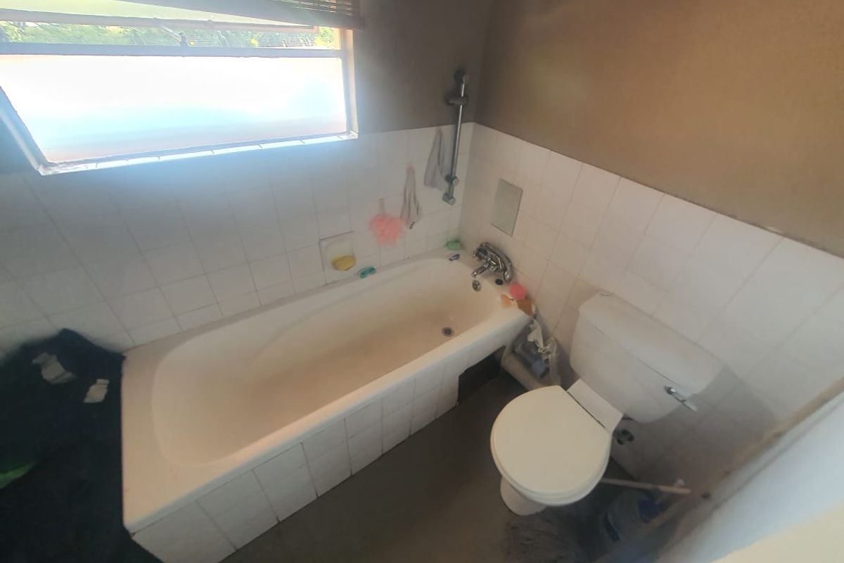A functional bathroom featuring a built-in bathtub, toilet, and tiled splashback, requiring cosmetic updates to modernize the space.
