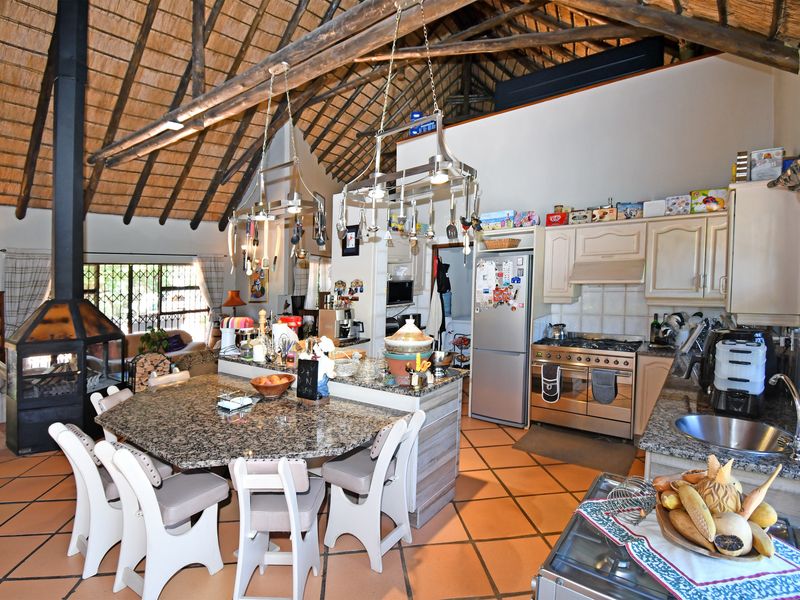 Spacious open-plan living and kitchen area featuring a high vaulted thatch ceiling with exposed timber beams, a central fireplace, and granite kitchen countertops.