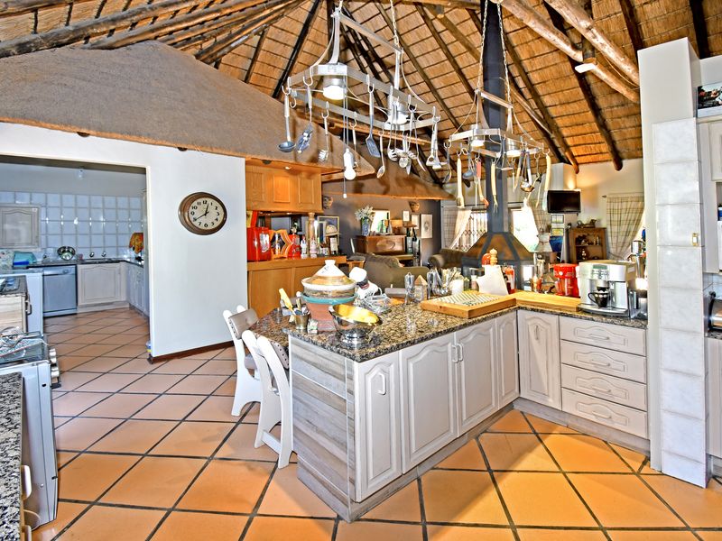 Spacious open-plan kitchen and living area featuring a traditional thatched roof, exposed timber rafters, granite-topped island, and a central fireplace.