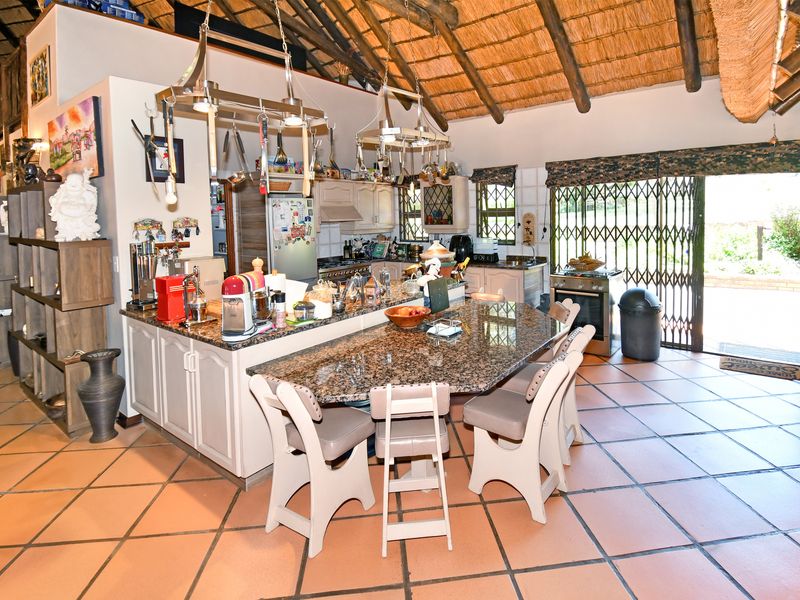 Spacious farmhouse kitchen featuring a large granite-topped island, tiled flooring, and a high vaulted thatch ceiling with exposed timber beams.
