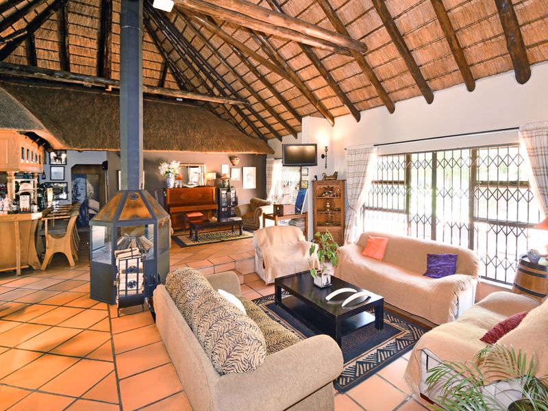 Spacious open-plan living area featuring a high thatched roof with exposed timber rafters, a central freestanding fireplace, and a built-in bar area.