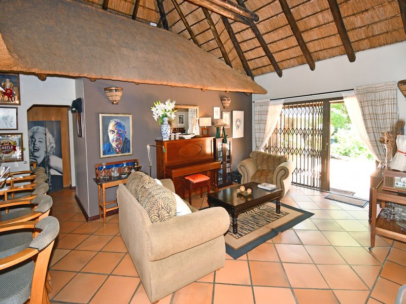 Spacious living area featuring a traditional thatched roof with exposed timber rafters, terracotta tiled flooring, and direct access to the garden through sliding doors.