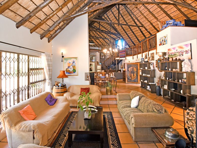 Spacious open-plan living area featuring a high vaulted thatched ceiling with exposed timber trusses, mezzanine level, and terracotta tiled flooring.