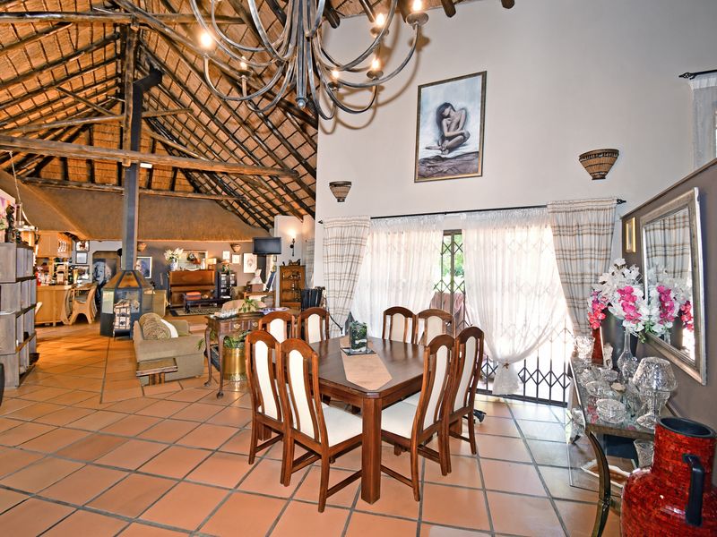 Spacious open-plan living and dining area featuring a high exposed thatch roof, terracotta tiling, and a central freestanding fireplace.