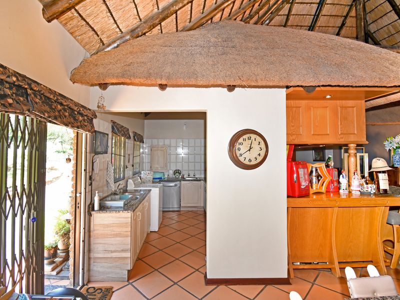 A functional scullery area featuring tiled flooring, built-in cabinetry, and a stainless steel sink, situated adjacent to the main living space under a thatched roof.