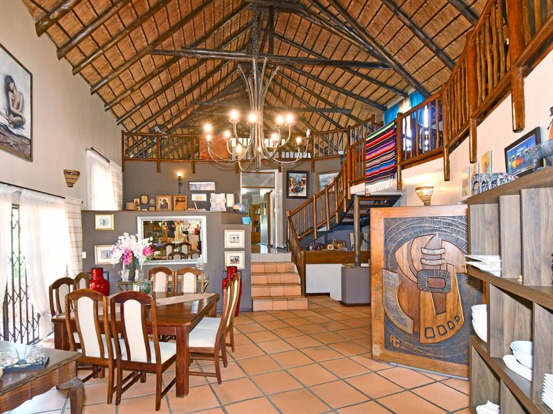 Spacious open-plan living and dining area featuring a high vaulted thatched ceiling with exposed timber trusses, a mezzanine level, and terracotta floor tiles.