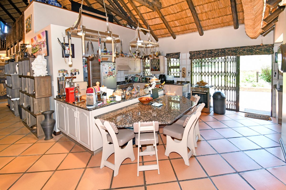 Spacious farmhouse kitchen featuring a large granite-topped island, tiled flooring, and a high vaulted thatch ceiling with exposed timber beams.