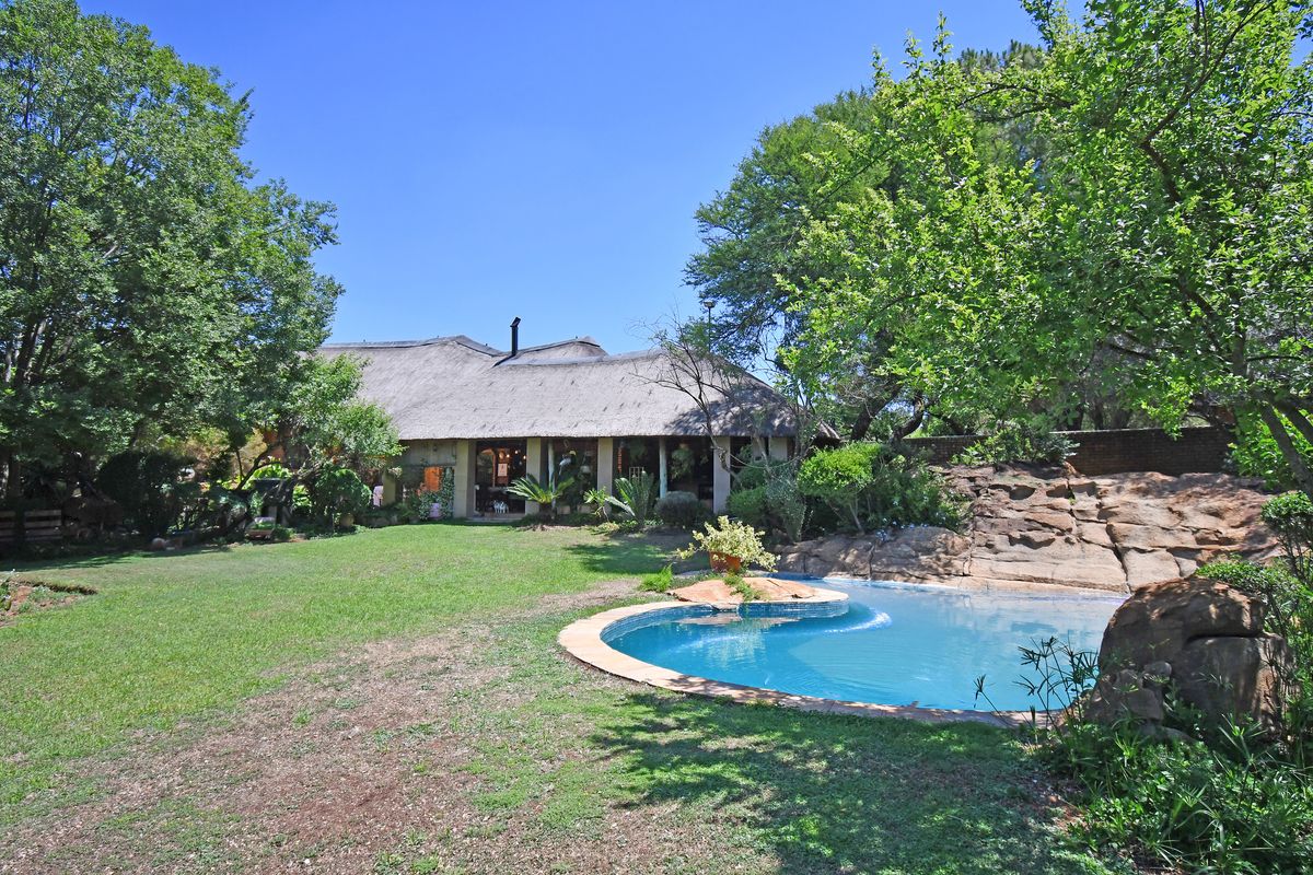 Rear view of a farm-style property featuring a thatched roof dwelling, a landscaped garden, and a natural rock-style swimming pool.