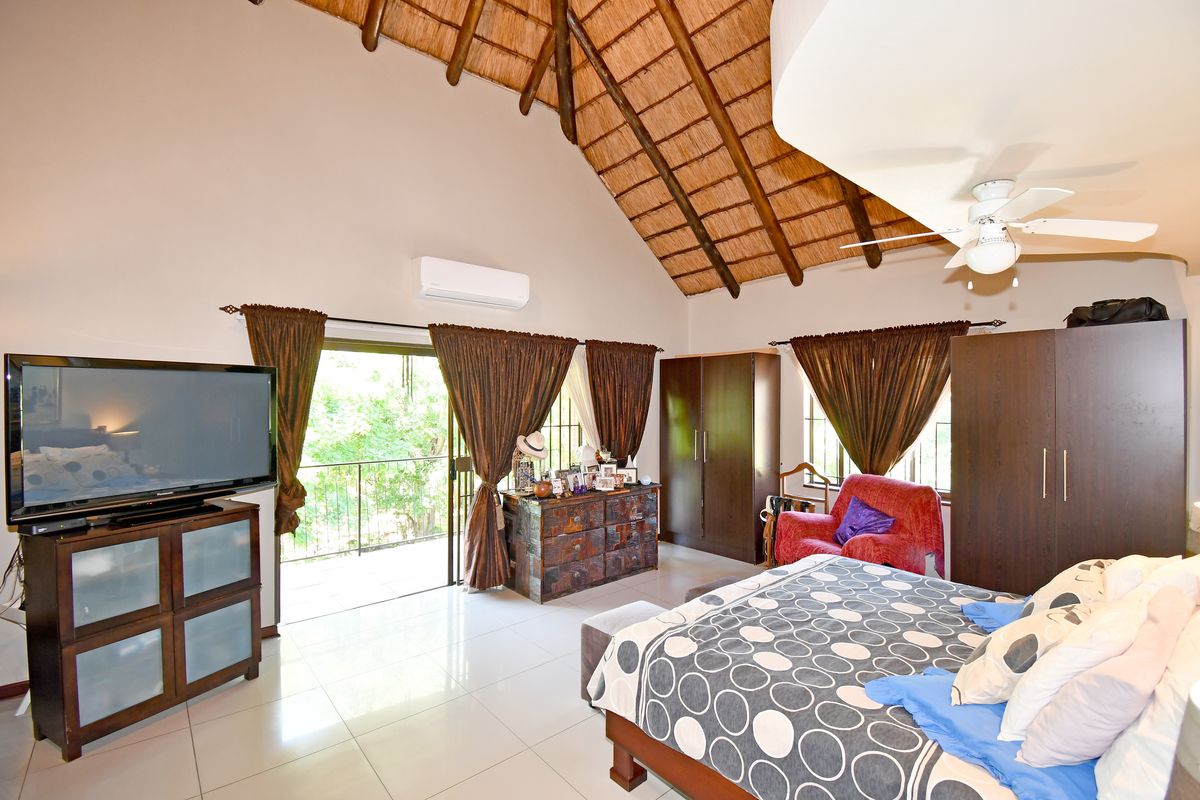 Spacious bedroom featuring a high vaulted thatched ceiling with exposed timber rafters, tiled flooring, and direct access to a private balcony.