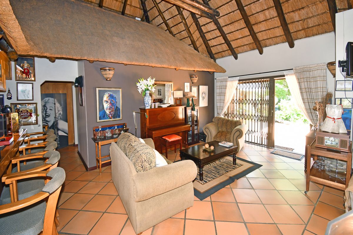 Spacious living area featuring a traditional thatched roof with exposed timber rafters, terracotta tiled flooring, and direct access to the garden through sliding doors.