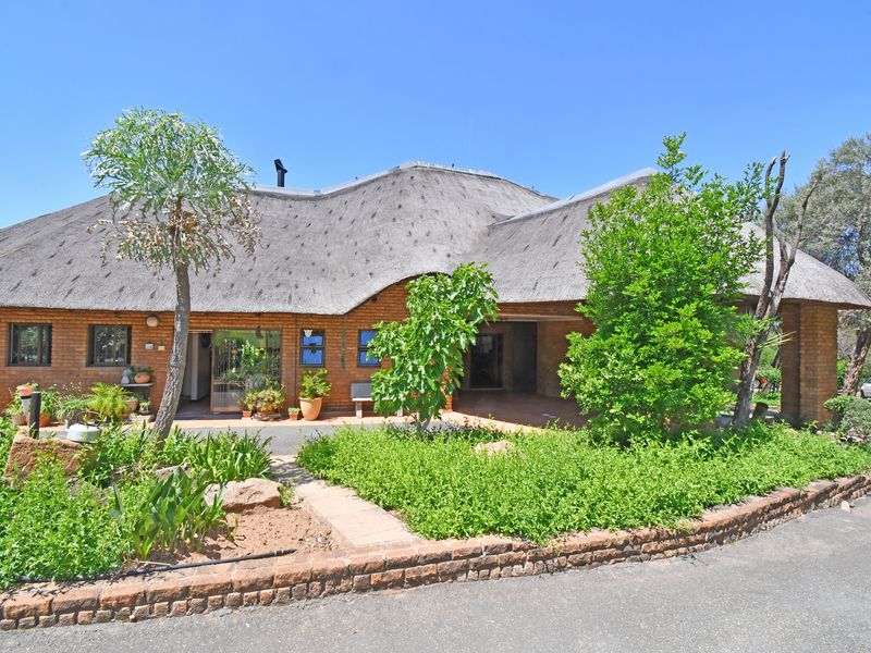 Front elevation of a traditional farm-style residence featuring a distinctive thatched roof, face brick exterior, and established garden landscaping.