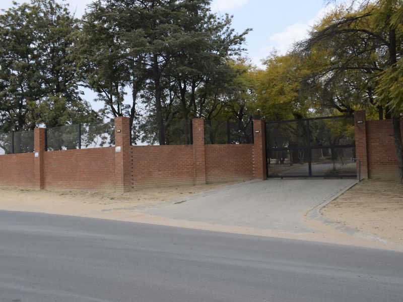 Street view of the property entrance featuring a secure brick boundary wall, metal gate, and paved driveway access.