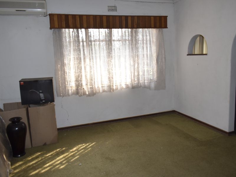 An empty living room featuring an archway, a wall niche, and an air conditioning unit, with visible wear to the carpet and wall finishes.
