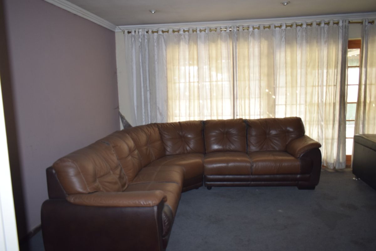 A living room featuring recessed lighting, coving, and a sliding glass door with curtain tracks. The wall corner shows visible damage.