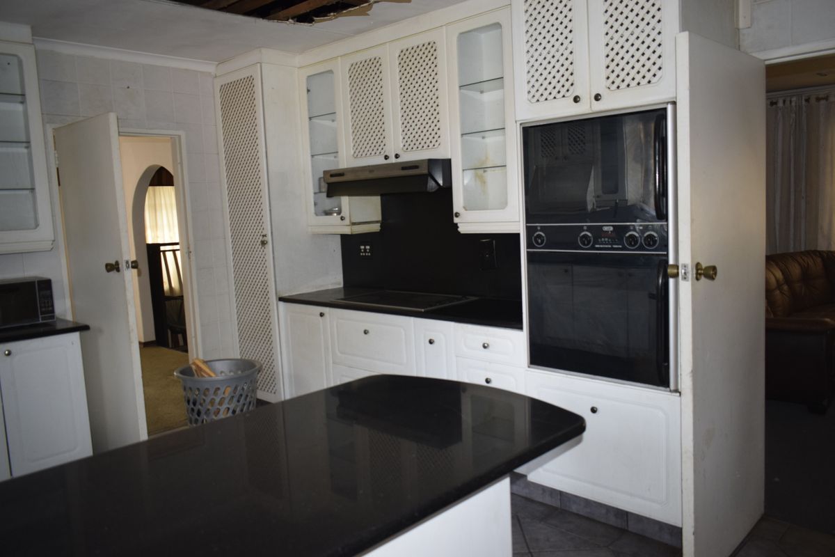 A dated kitchen featuring black granite countertops, built-in cabinetry, and integrated appliances, currently requiring ceiling repairs.