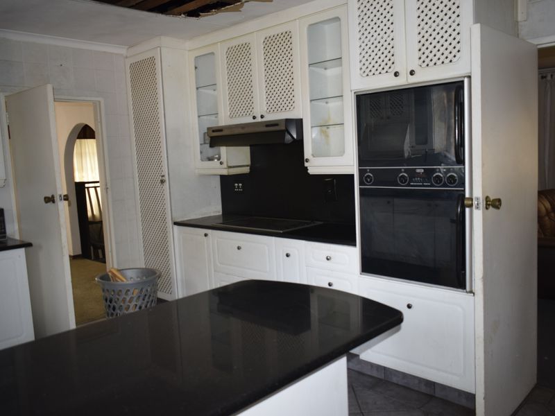 A dated kitchen featuring black granite countertops, built-in cabinetry, and integrated appliances, currently requiring ceiling repairs.