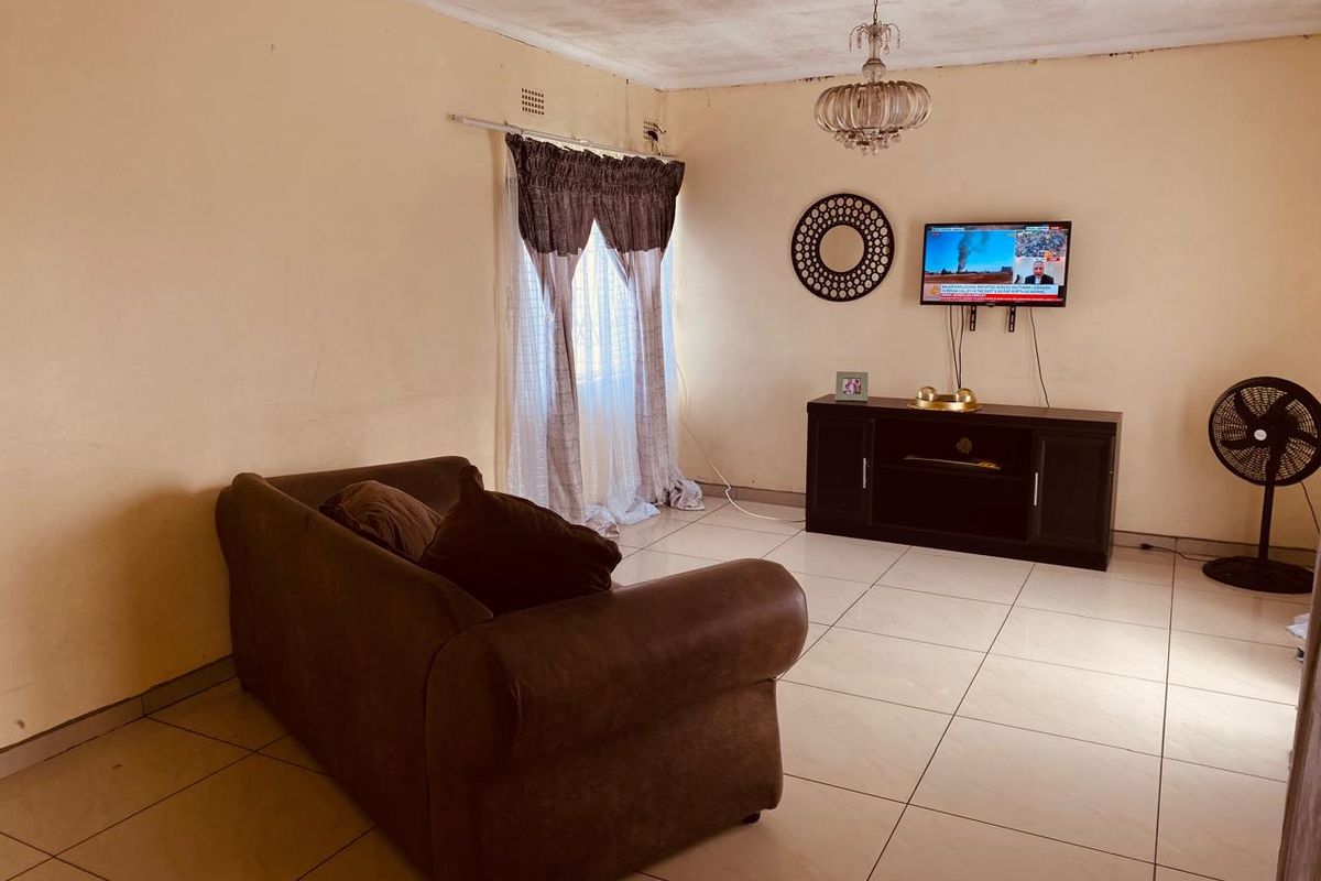 A living room featuring tiled flooring and a central chandelier, requiring cosmetic updates to the ceiling and wall finishes.