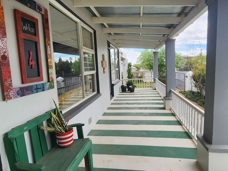 A covered front patio featuring a painted striped concrete floor, support columns, and a railing, providing a welcoming entrance area to the home.